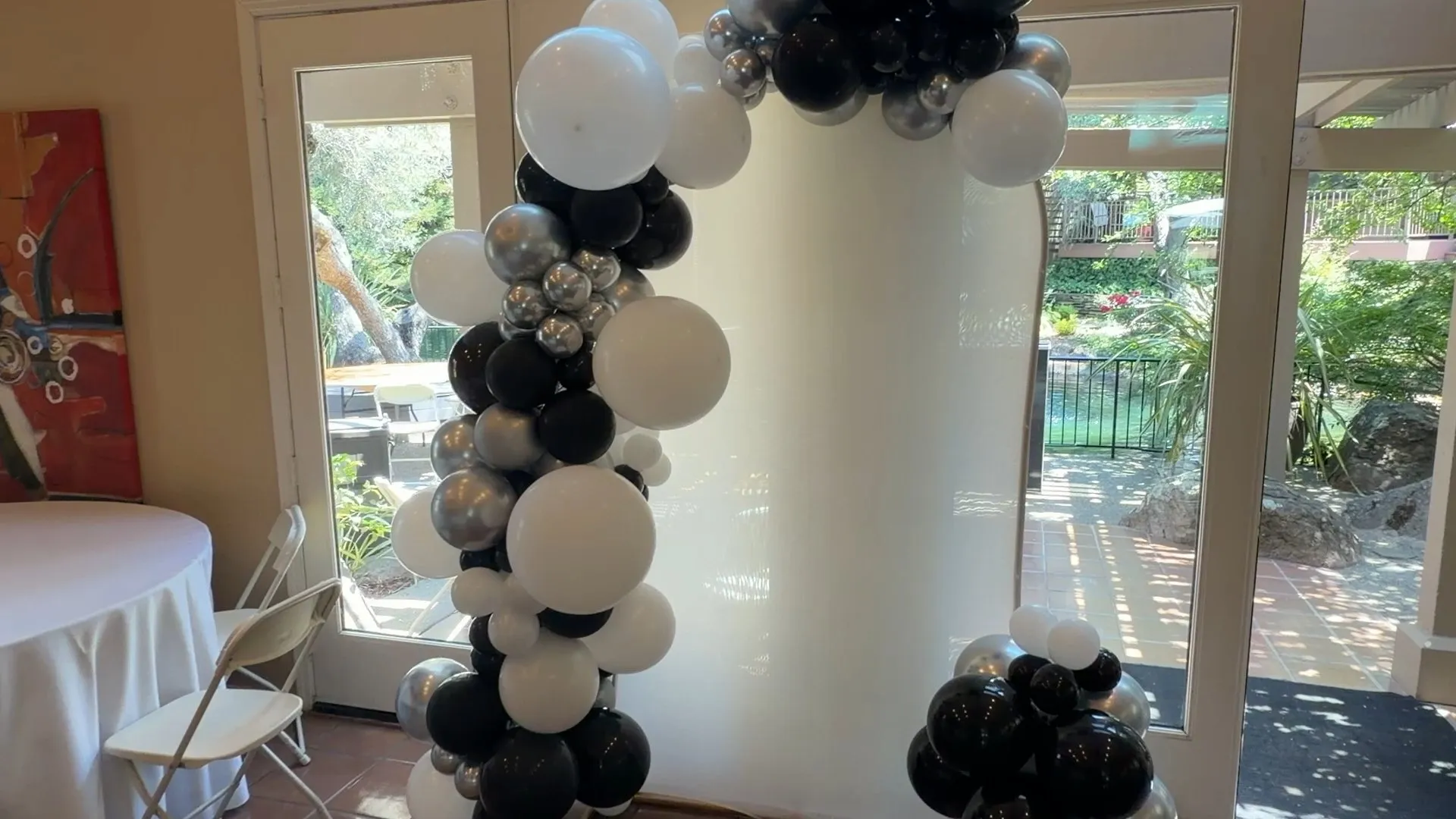 Black, white and chrome silver organic balloon garland installed around an arched clubhouse entryway with banquet tables set behind it